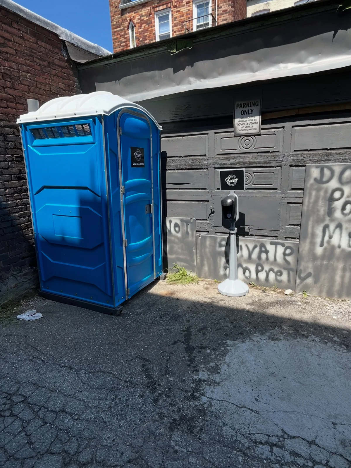 Blue portable toilet and freestanding sanitizer dispenser beside a building