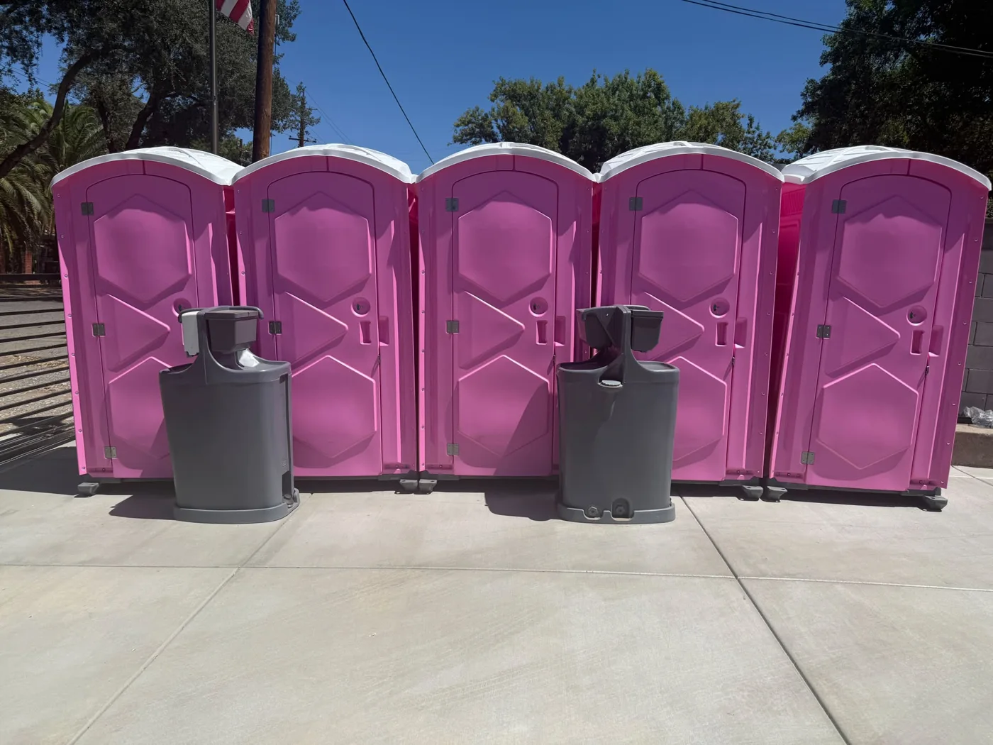Five pink portable toilets with two separate handwashing stations